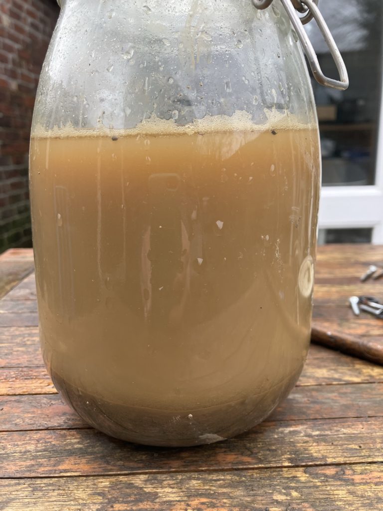 A glass jar filled with brown water that is mostly clay suspended in the water, with sand at the bottom in a much thinner layer